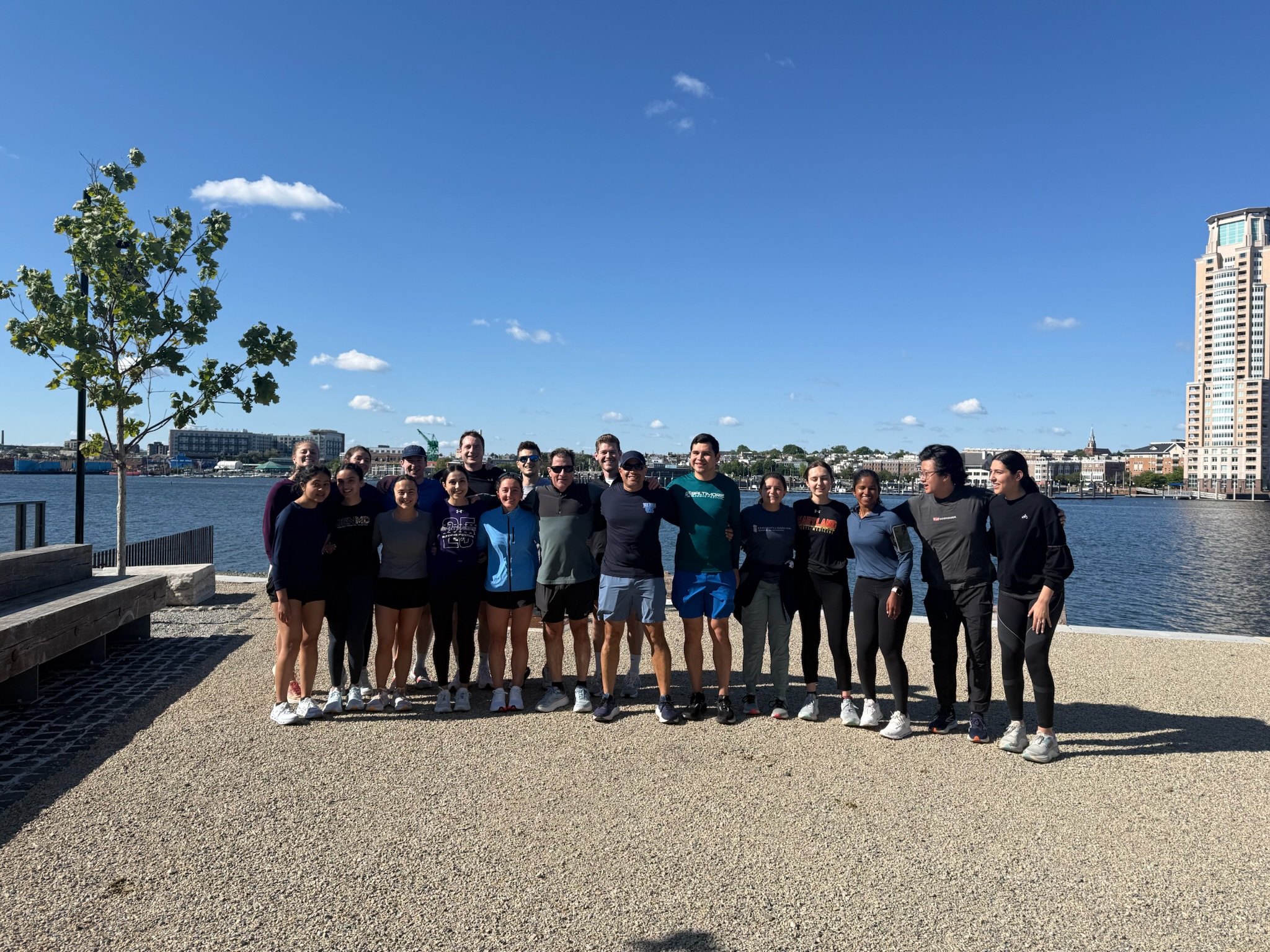 Dean Gladwin and Dr. Shah join the UMSOM run club and pose for a group photo along Baltimore's Inner Harbor on a sunny day.